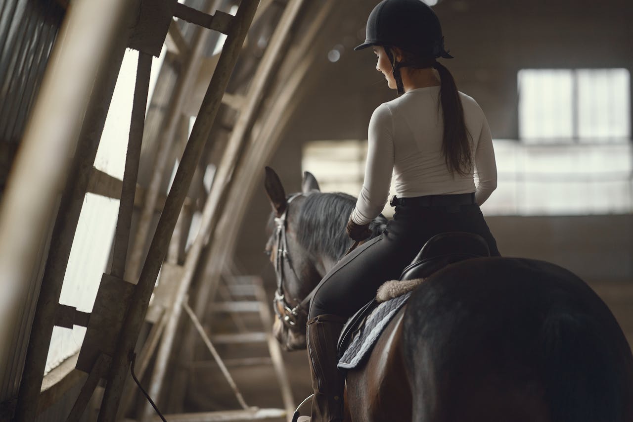 about-us A female equestrian riding a horse indoors, focusing on dressage training.