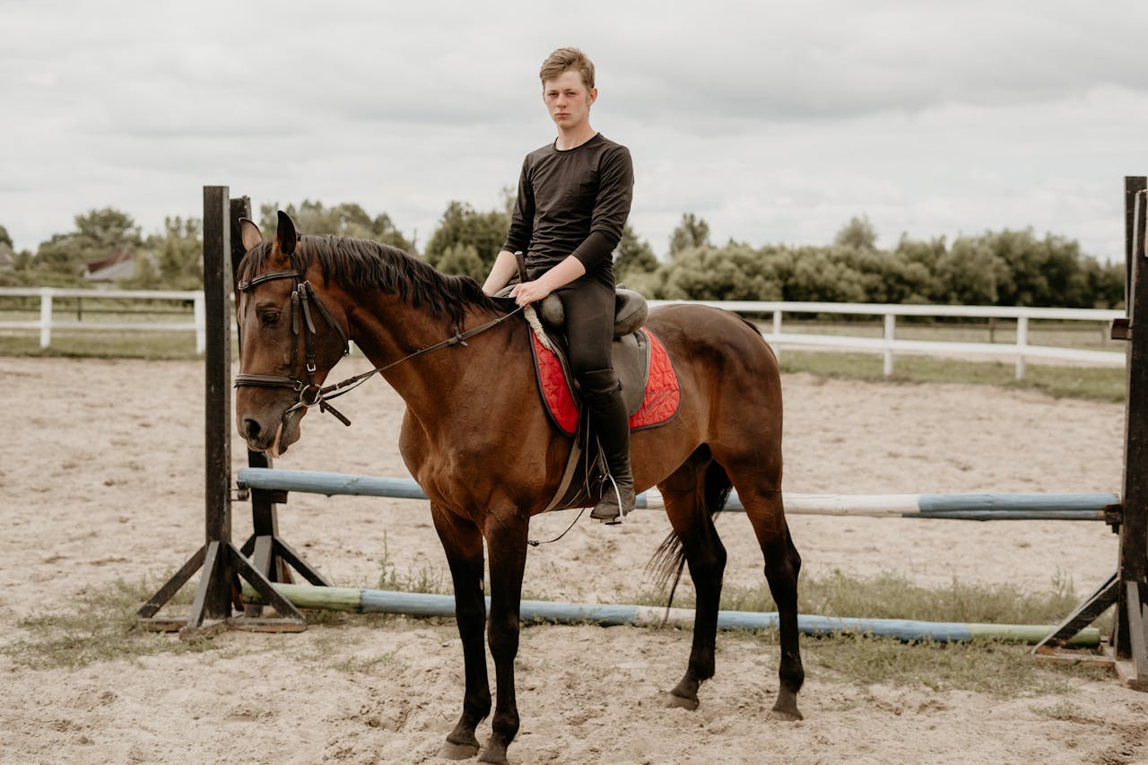 A young man sits confidently on a horse in an outdoor equestrian arena.